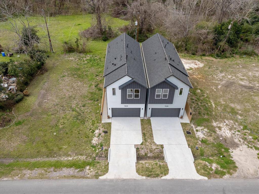 This aerial view shows two modern home designs. Each home has a fenced backyard and a paved driveway leading to the street. The homes are situated on a spacious plot with ample green space surrounding them.