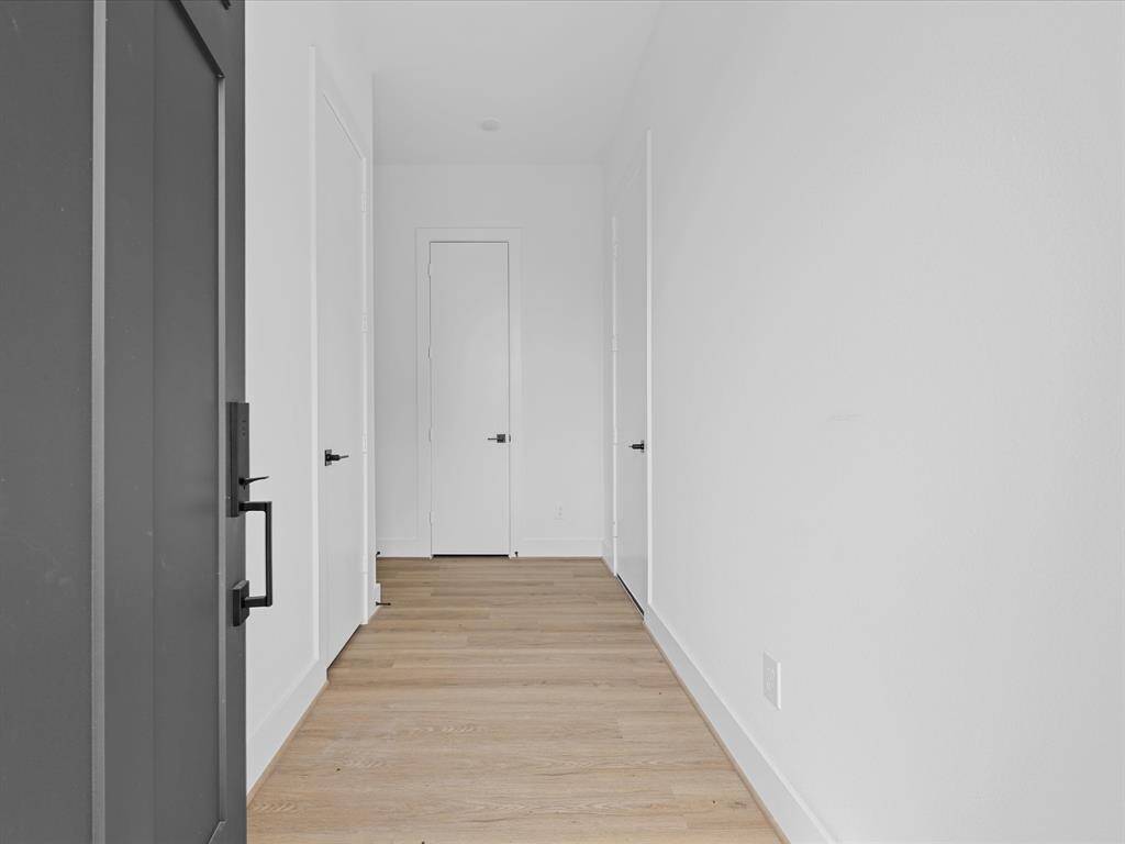 This photo showcases a modern home's entrance with a sleek dark door and white siding. The exterior is well-maintained, with a paved walkway leading to the door, offering a clean, contemporary look.