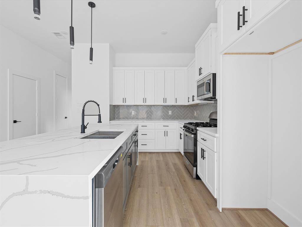 Modern kitchen with sleek white cabinetry and a stylish herringbone backsplash. Features a spacious island with marble-like countertops, black fixtures, and pendant lighting. Bright, open layout with hardwood flooring.