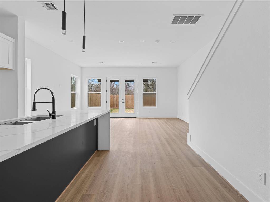 This modern kitchen features sleek white cabinetry, a large marble-patterned island with a built-in sink, stainless steel appliances, and stylish pendant lighting. The elegant herringbone backsplash adds a touch of sophistication, while the light wood flooring complements the bright, open space.