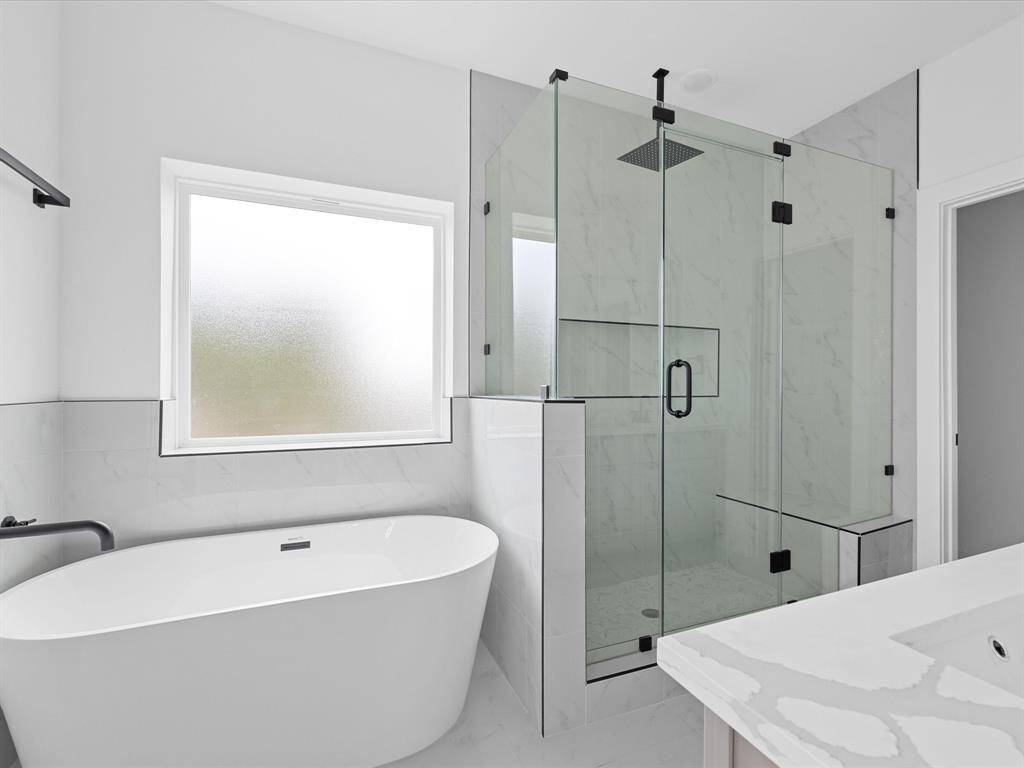 This modern bathroom features a sleek freestanding bathtub, a spacious glass-enclosed shower, and elegant marble-style tiles, offering a luxurious and bright space for relaxation.