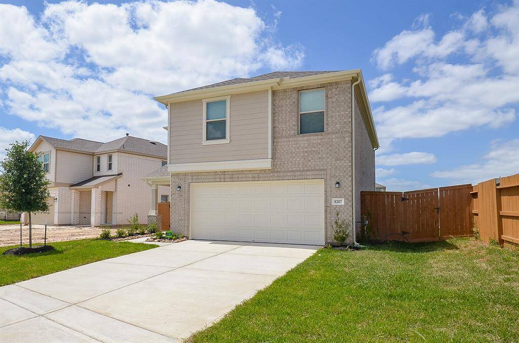 This is a modern two-story home with a light brick exterior and a two-car garage. It features a well-maintained front yard, a wooden fence for privacy, and a spacious driveway. The neighborhood appears clean and suburban.