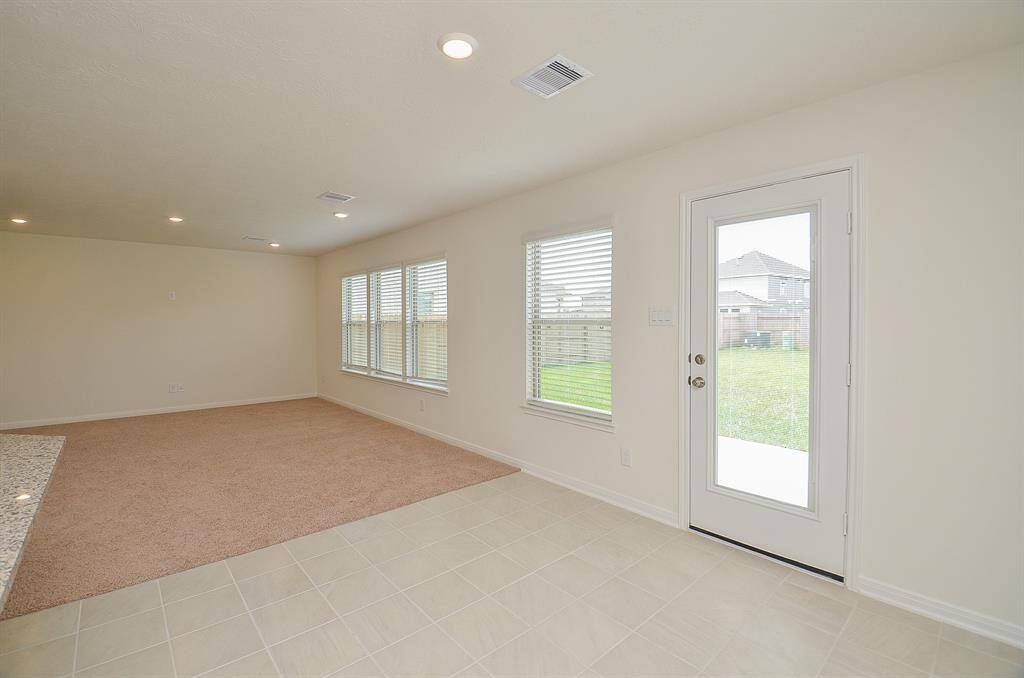 Bright, open living space with neutral tones, featuring a mix of carpet and tile flooring. Large windows and a glass door provide ample natural light and access to a fenced backyard.