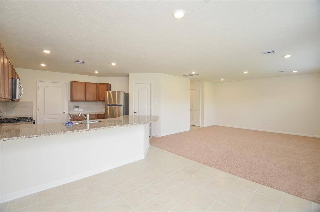This photo showcases a spacious, open-plan kitchen and living area. The kitchen features granite countertops, stainless steel appliances, and wooden cabinets. The living space has carpeted flooring, recessed lighting, and neutral walls, providing a versatile canvas for personalization.