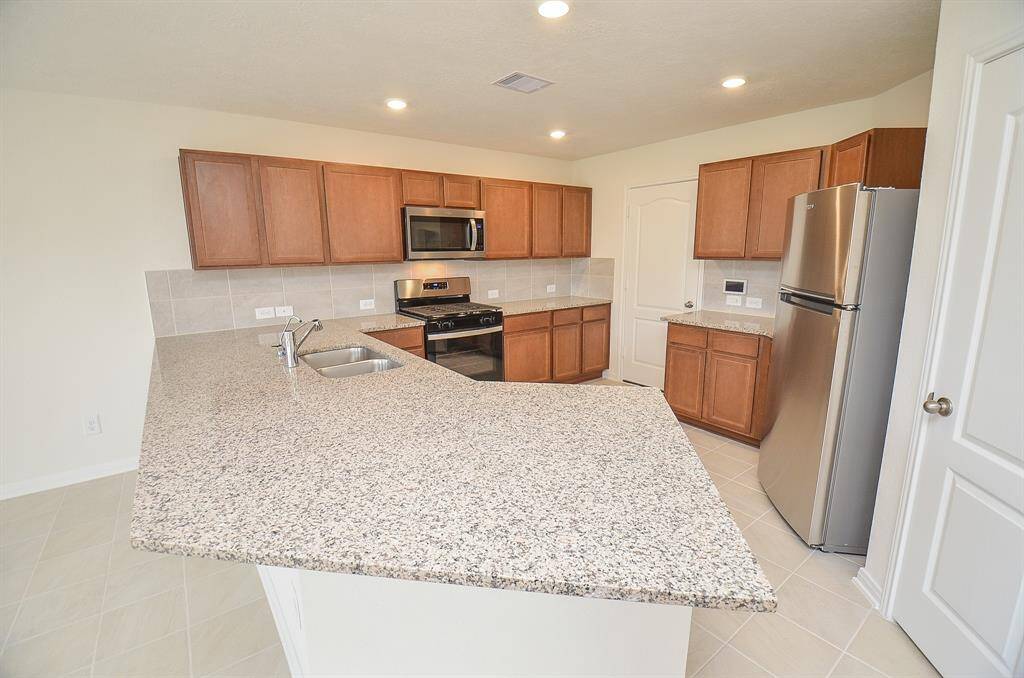 Modern kitchen with granite countertops, stainless steel appliances, and ample wooden cabinetry. Features a central island with a dual sink and a bright, open layout.