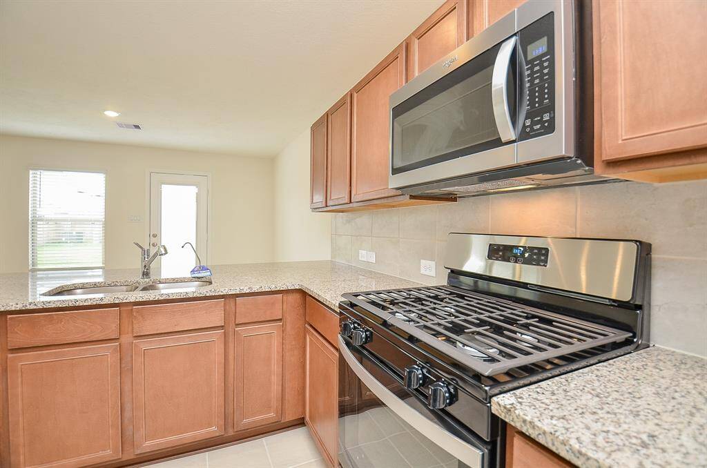 This photo shows a modern kitchen with granite countertops, stainless steel appliances, and wooden cabinetry. The space is bright with a window and door leading outside, offering ample natural light.