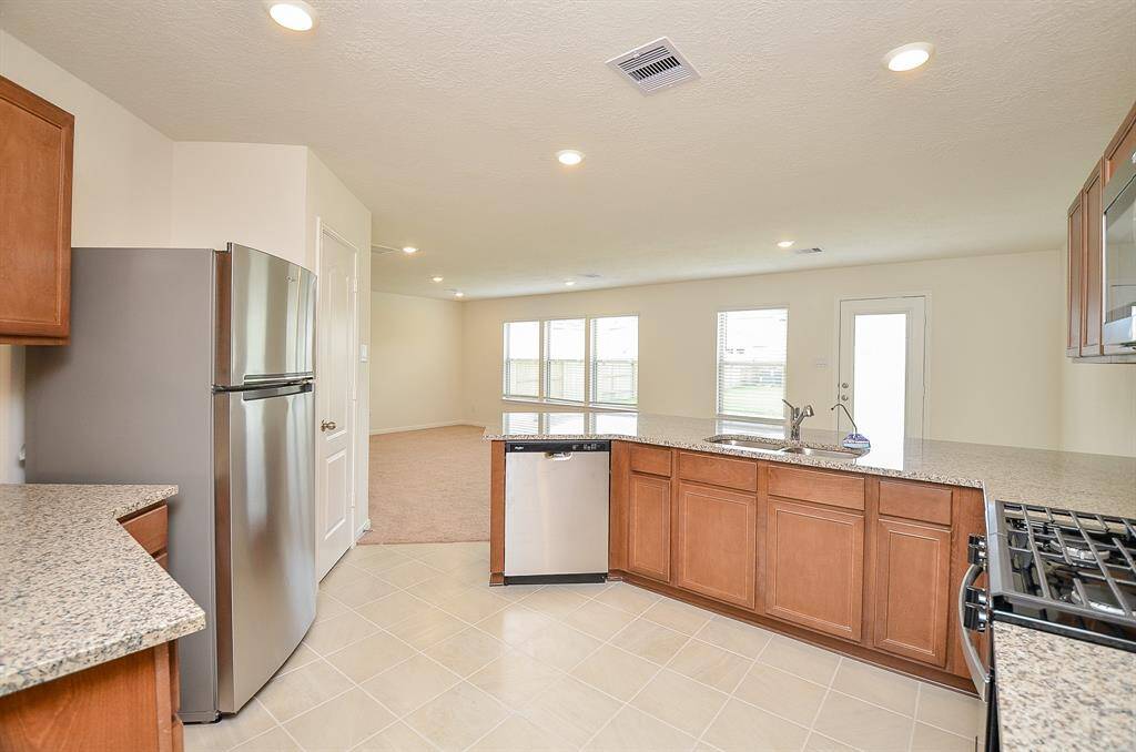 This modern kitchen features granite countertops, stainless steel appliances, and ample cabinet space. It opens to a spacious, light-filled living area with large windows and a door leading to the backyard.