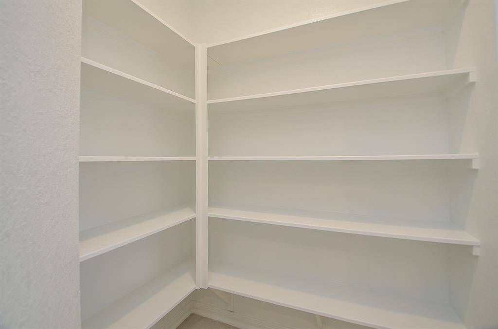 This photo shows a spacious walk-in pantry with multiple white shelves, ideal for organized storage.