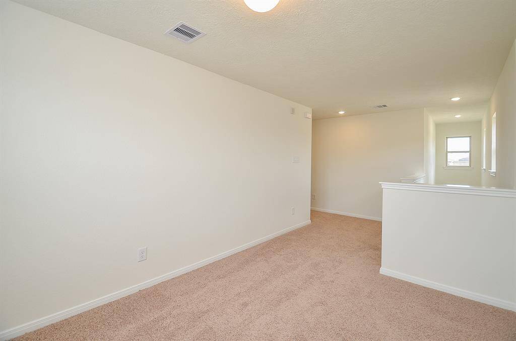 This photo shows the Game room upstairs with a bright, open hallway with neutral carpet and walls. It features recessed lighting, a small window for natural light, and a half-wall railing overlooking the stairs.