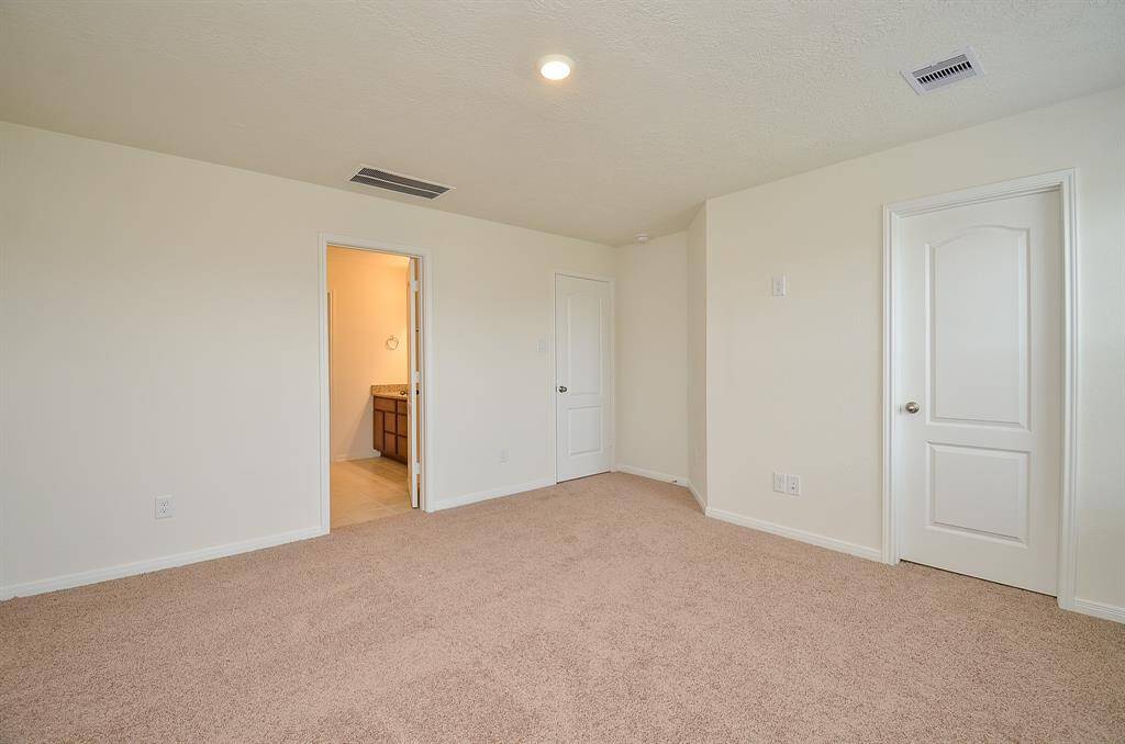 This is another view of the bright, spacious Primary bedroom with neutral carpet and walls, featuring two white doors—one leading to a bathroom and the other likely to a closet.