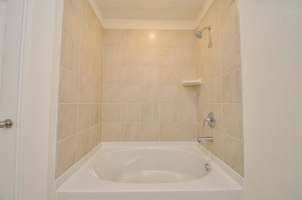 This photo shows a clean, modern Primary bathroom with a tub and shower combination, featuring neutral beige tiles and a built-in corner shelf.