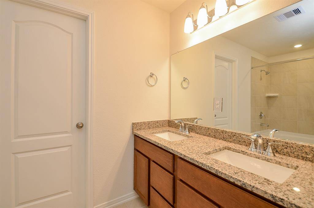 This Primary bathroom features a double sink with granite countertops, wooden cabinetry, and a large mirror. It has modern lighting fixtures and a separate shower area, creating a bright and functional space.