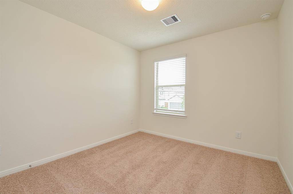 This is a well-lit second Bedroom with neutral walls and carpeted flooring. It features a window with blinds and a ceiling light.