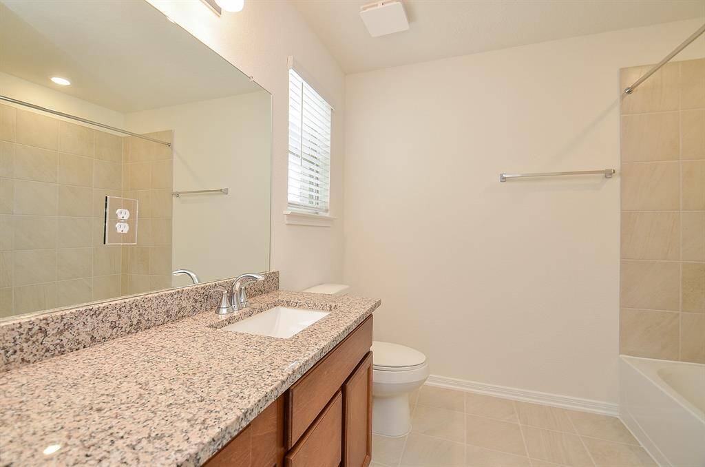 This second Full bathroom features a granite countertop with an under-mount sink, a large mirror, and a tub-shower combo. The space is bright and airy with neutral tile flooring and walls.