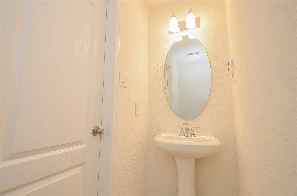 A compact, well-lit Powder room with a pedestal sink and oval mirror, featuring a simple light fixture and a towel ring.