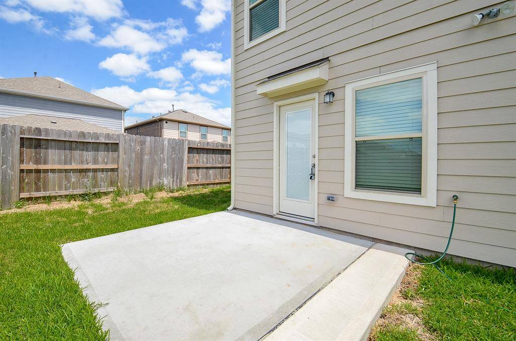 This photo shows the backyard with a concrete patio area, surrounded by a wooden fence. The exterior features beige siding with a glass door and a window, offering a neat space for outdoor relaxation.
