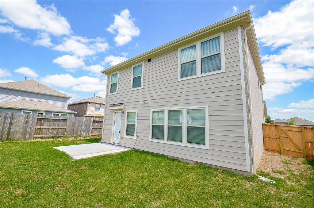 This photo features the backyard of a two-story house with light-colored siding, a small concrete patio, and a fenced lawn, offering a private outdoor space.