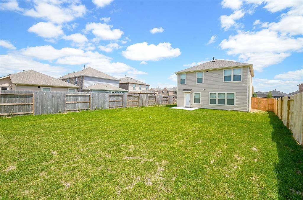 Spacious backyard with a well-maintained lawn, surrounded by wooden fencing. The two-story house features modern siding and multiple windows, providing ample natural light. Ideal for outdoor activities and gatherings.