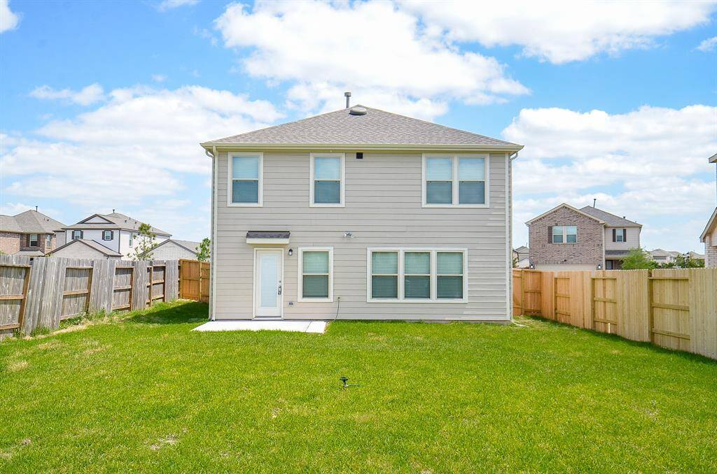 This photo shows the back of a two-story house with light siding, a small concrete patio, and a spacious fenced backyard. Ideal for outdoor activities and privacy, it offers a clear view of a bright, open sky.
