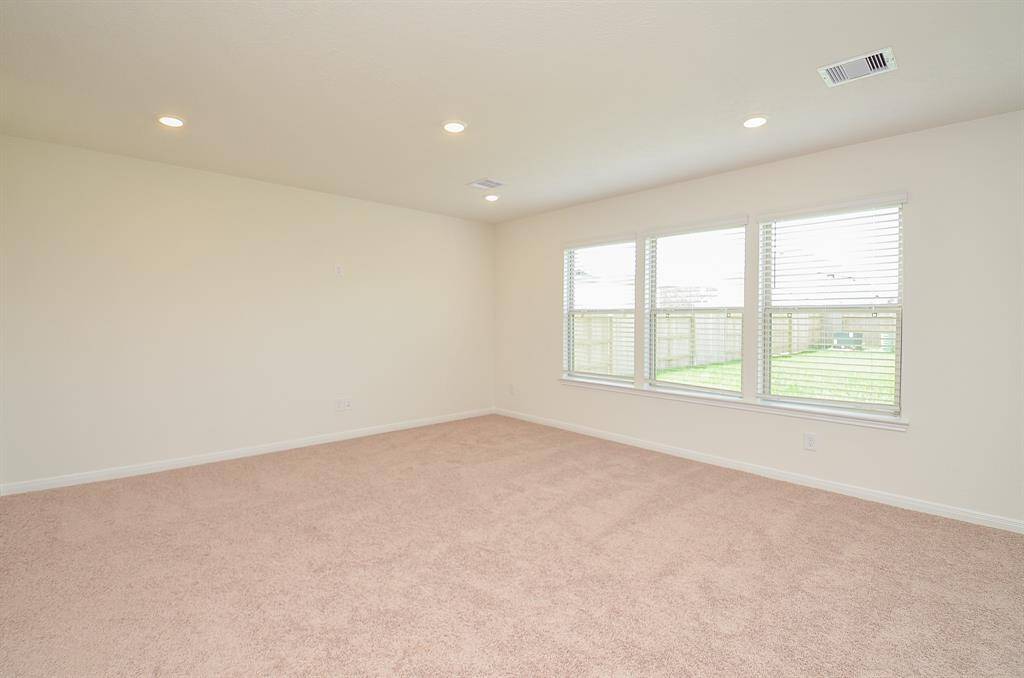 This room is spacious with neutral walls and carpet, featuring large windows that provide ample natural light and a view of the fenced backyard. Recessed lighting adds a modern touch.