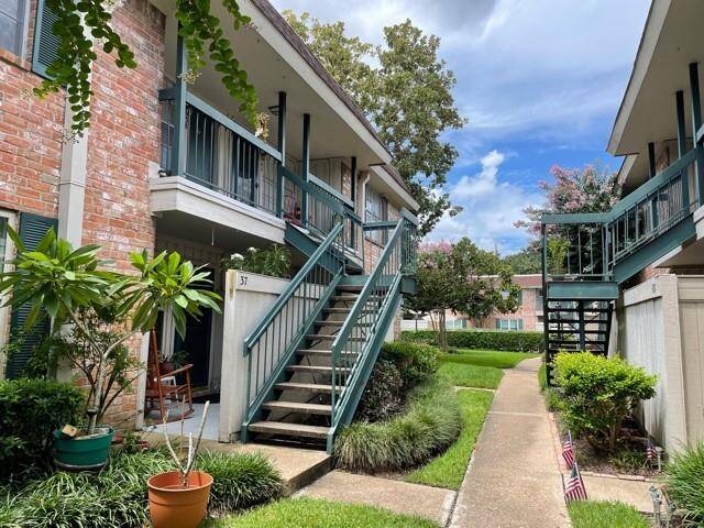 Charming condo complex with brick exteriors and green accents. It features two levels connected by outdoor staircases, surrounded by well-maintained landscaping. The setting is inviting and boasts a peaceful atmosphere.