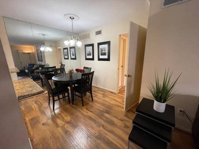 Dining area features laminate-wood flooring. A large mirror and contemporary chandelier enhance the space, while wall art adds a touch of elegance. The area connects smoothly to a cozy living room.