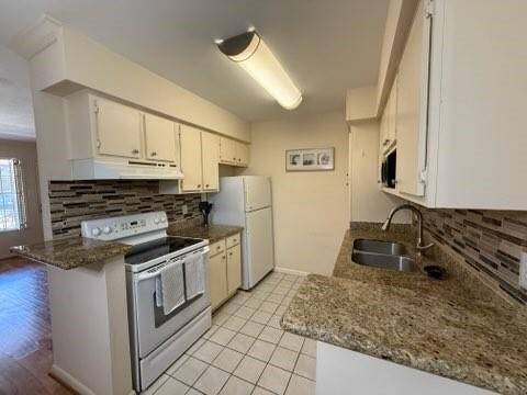 Kitchen features granite countertops and a stylish tile backsplash. It includes white cabinets, a white stove, and a refrigerator. The space is well-lit and opens to an adjacent living area with wood flooring.