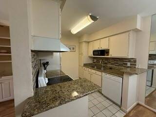 This kitchen features granite countertops, white cabinetry, and tile flooring. It includes modern appliances, with a microwave, and a tiled backsplash, offering a clean and functional space.