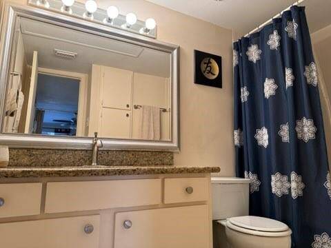 Bathroom features a granite countertop with a single sink, a large, framed mirror with ample lighting. The decor is simple with light cabinetry and a modern feel.