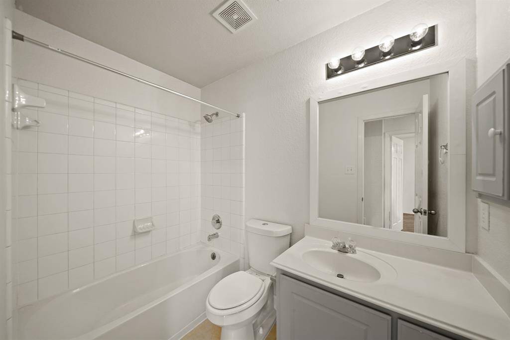 Stunning secondary bathroom featuring a shower/tub combo with a tile wall, tile flooring, white cabinets and granite countertops, a large mirror and vanity lights.
