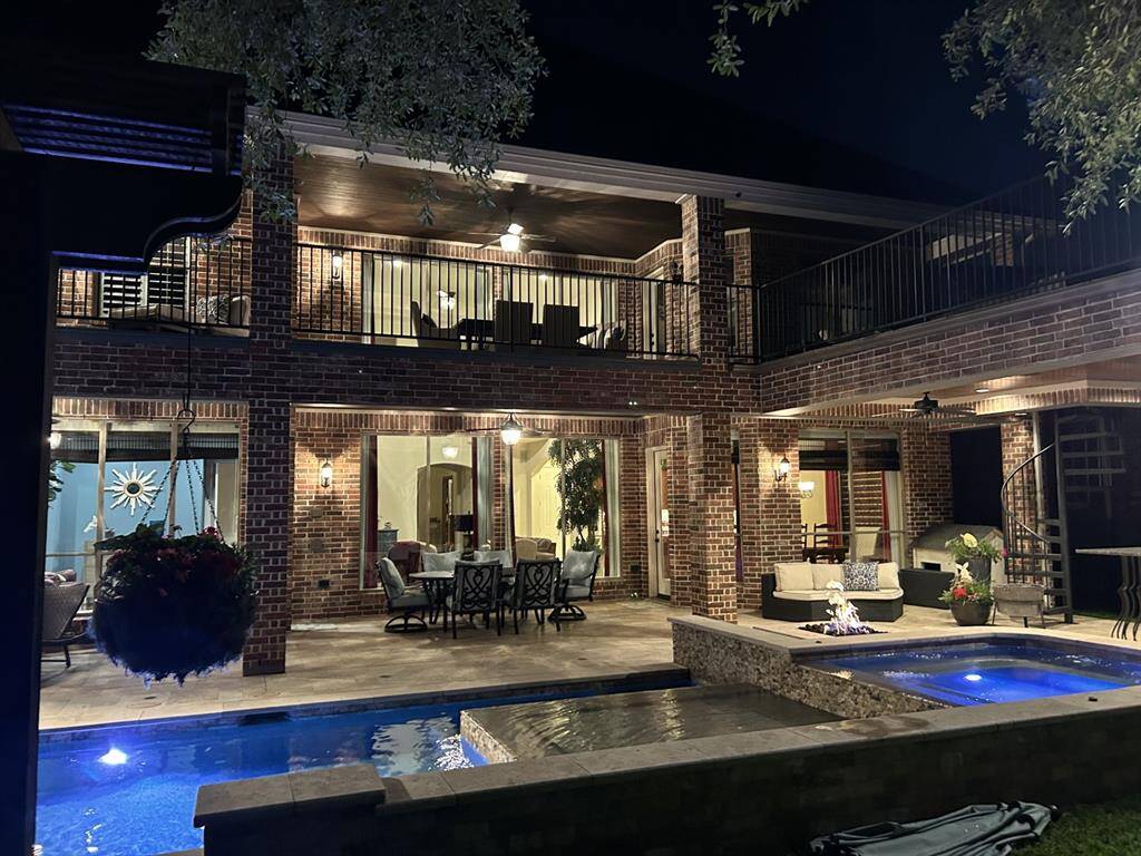 A beautiful night view of the pool/firepit/spa and the lit up balcony and covered porch area.