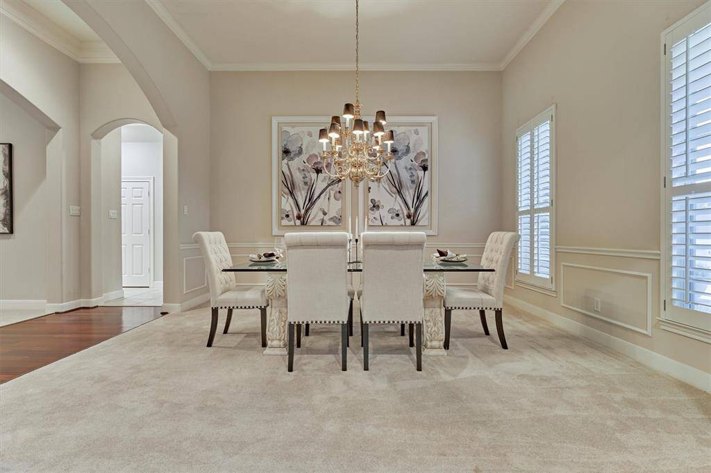 The spacious dining room features an elegant chandelier, plantation shutters and plush carpeting.
