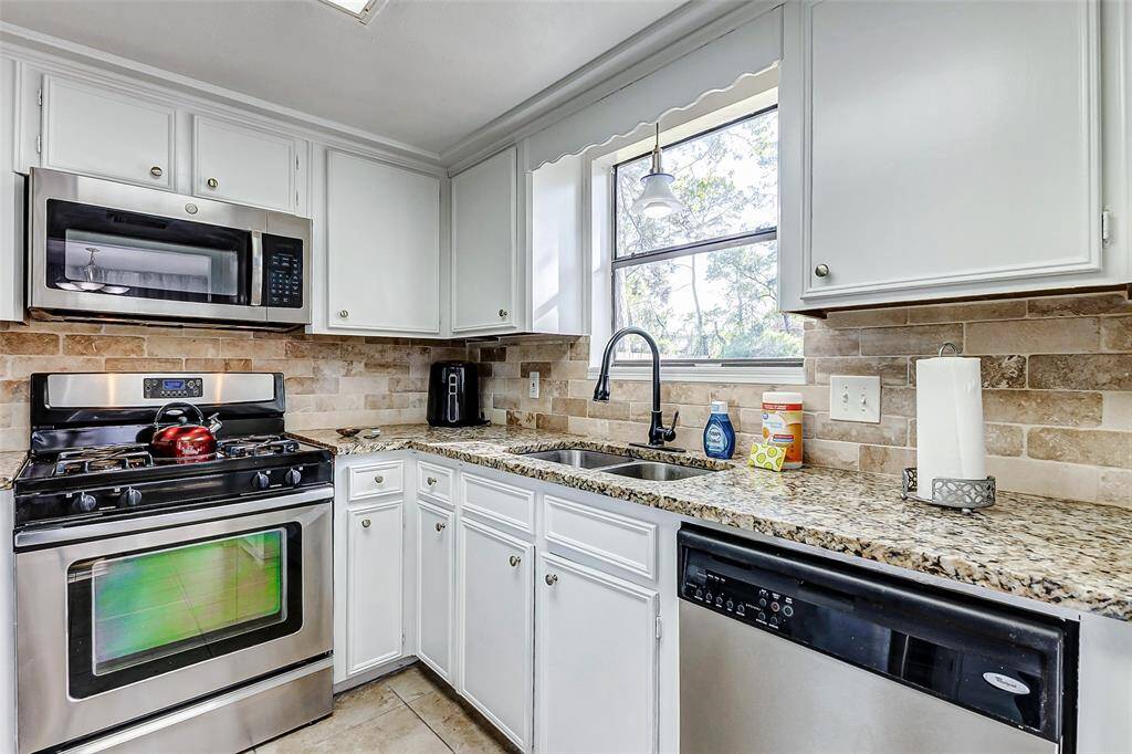This kitchen features modern stainless steel appliances, granite countertops, and white cabinetry. A window above the sink provides natural light, and the warm-toned tile backsplash adds a cozy touch.