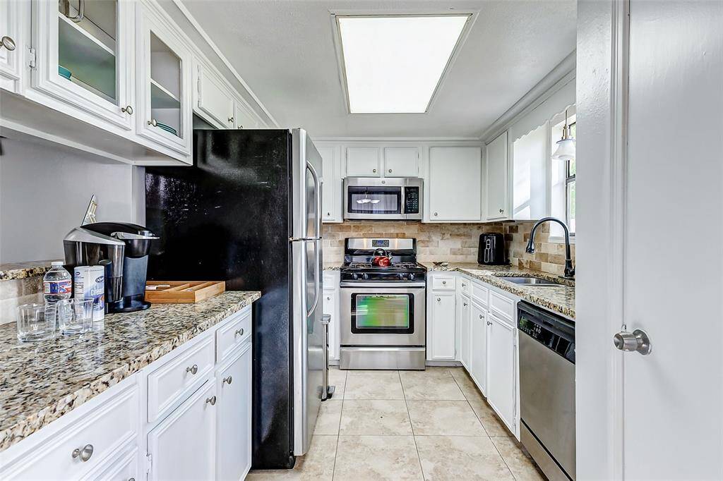 This kitchen features modern stainless steel appliances, granite countertops, and ample white cabinetry. The layout is efficient with a cozy atmosphere, enhanced by natural light from a window above the sink.