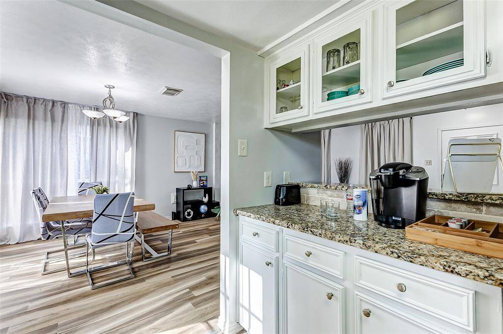 The photo showcases a bright dining area with modern decor and wooden flooring, adjacent to a kitchen with granite countertops and white cabinetry. The space is airy and well-lit, offering a cozy yet stylish atmosphere for dining and entertaining.