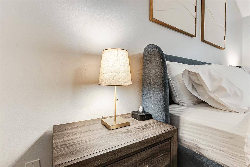 This photo features a cozy bedroom setup with a modern bedside table and lamp, complemented by a cushioned headboard and neutral bedding. With charging station. Minimalist wall art adds a touch of elegance.