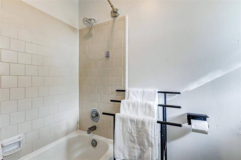 This bathroom features a classic white tile shower and tub combo, with a sleek towel rack and convenient toilet paper holder, offering a clean and functional space.