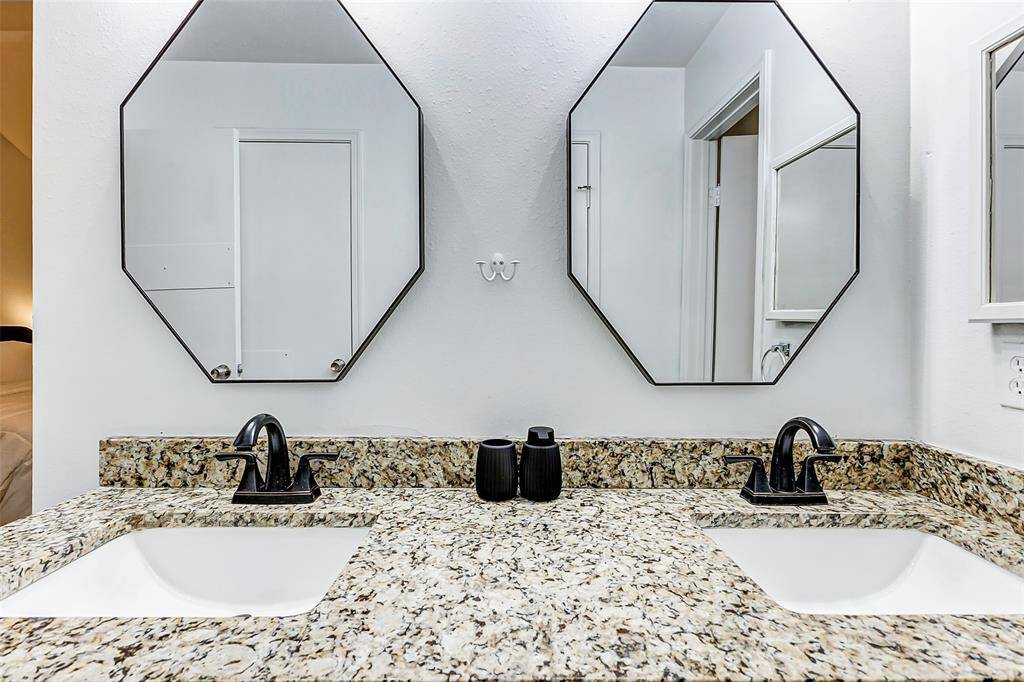 This bathroom features a double vanity with elegant granite countertops, modern black fixtures, and octagonal mirrors, offering a stylish and functional space.