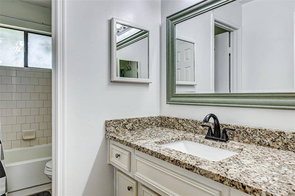 This photo showcases a modern bathroom with a granite countertop, sleek black faucet, and a large framed mirror. The space is bright, featuring white cabinetry and a tiled shower area visible through an open door.