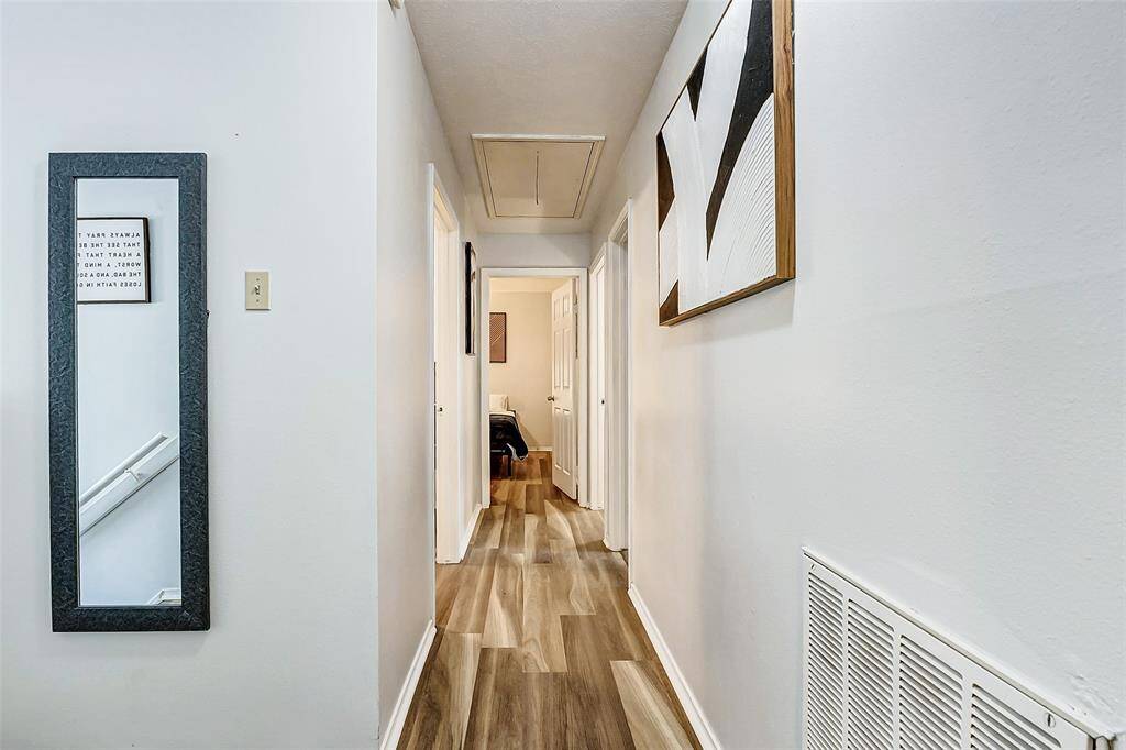 Bright, inviting hallway with modern wood-look flooring, neutral walls, and contemporary artwork, leading to multiple rooms.