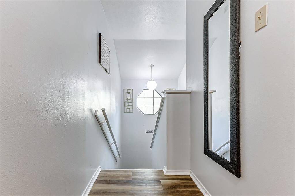 This photo showcases a bright, narrow stairway with sleek flooring and white walls. It features a modern light fixture, decorative wall art, and a large mirror, creating an inviting and spacious feel.