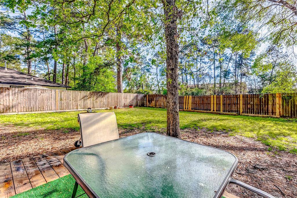 Spacious backyard with mature trees, a wooden patio, and a glass table. Perfect for outdoor relaxation and entertaining, surrounded by a privacy fence.
