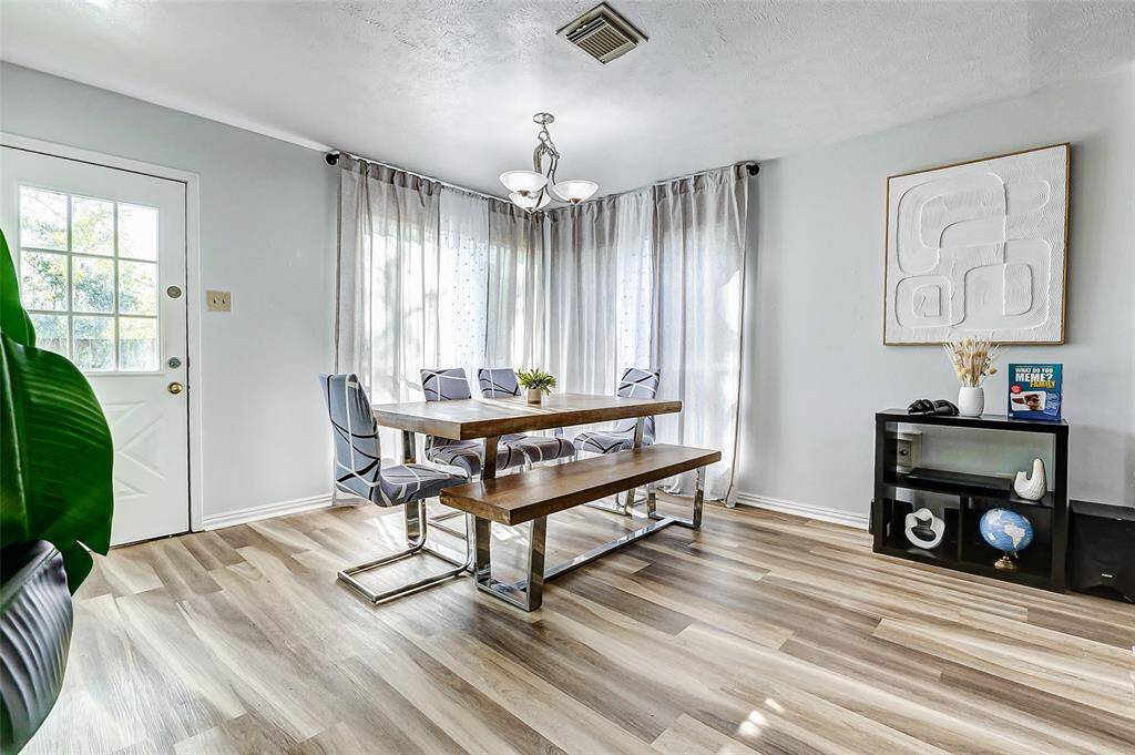 Bright dining area with modern furnishings, featuring a wooden table, sleek chairs, and large windows with sheer curtains. Neutral color floors and neutral walls create a spacious, inviting atmosphere.