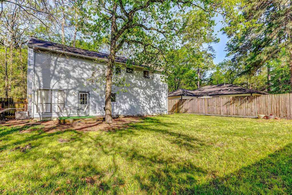 Spacious backyard with mature trees and a fenced perimeter, offering ample privacy. The house exterior is visible, with a simple, clean design and large windows for natural light. Ideal for outdoor activities and relaxation.