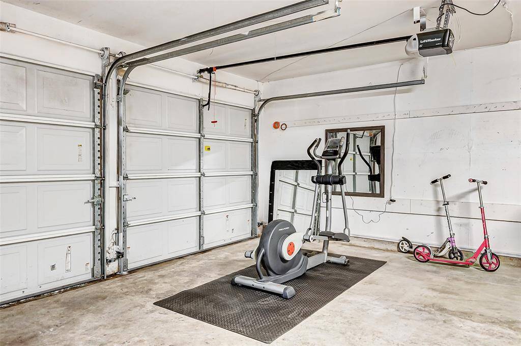 This spacious garage features two large doors, ample room for storage or a home gym, and includes an exercise machine and scooters. Ideal for versatile use and organization.