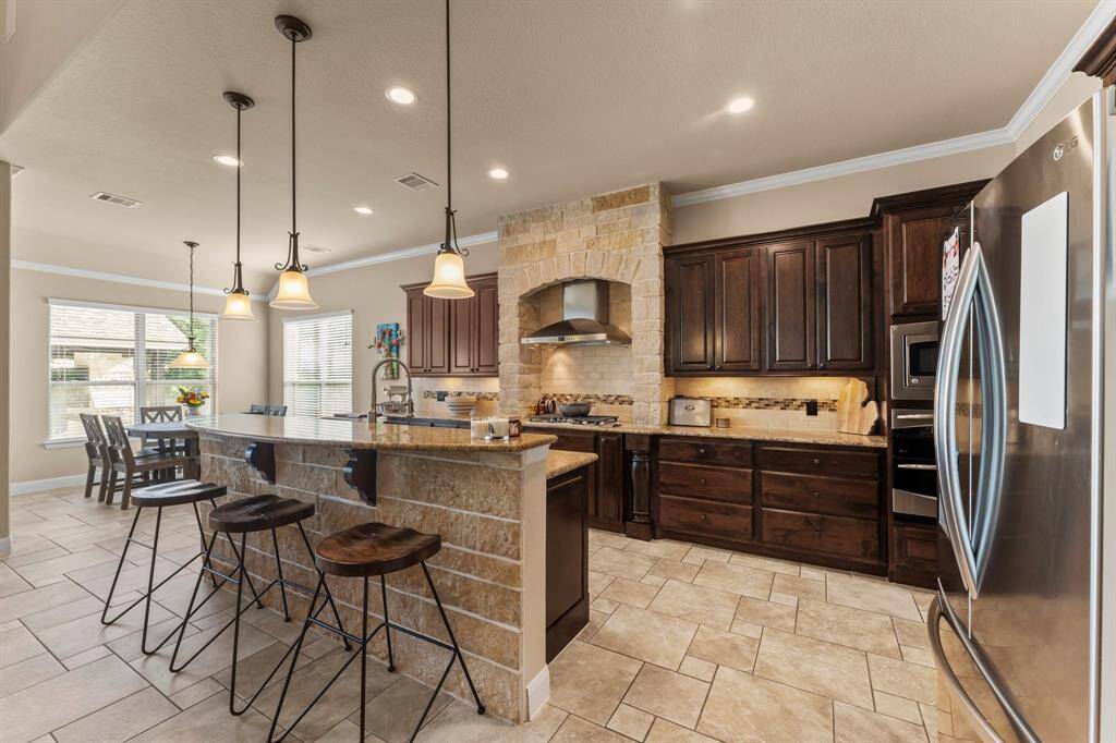 Gourmet chefs and home cooks alike will be inspired in this spacious kitchen, showcasing elegant Versailles tile flooring and a large island with curved breakfast bar seating. Sleek granite countertops, recessed lighting, crown molding, and stainless steel appliances add modern style, while thoughtful features like a pull-out trash/recycle drawer and deep drawers for pots and pans enhance functionality. There's plenty of space to create, gather, and enjoy.