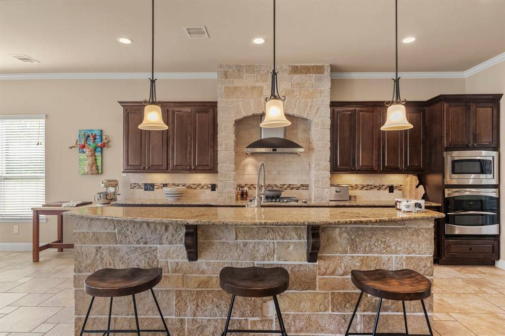 The centerpiece of the kitchen, this versatile island features sleek pendant lighting, breakfast bar seating, and extra cabinetry to keep everything organized. With generous prep space for the busy home chef, it’s both functional and stylish. Coordinating island stonework extends to the cooktop area, beautifully accenting the striking stainless steel vent hood.