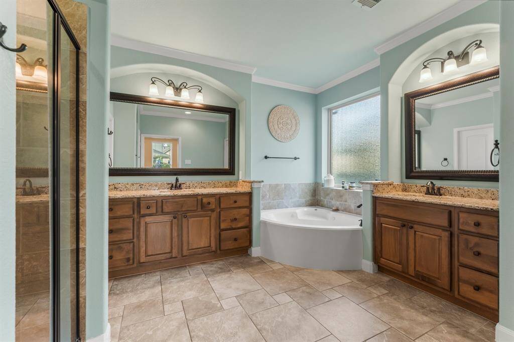 Designed as a true retreat, this luxurious en-suite bath offers both functionality and elegance—ideal for busy mornings or winding down before an evening out. A grand double-door entry leads to Versailles tile flooring, crown molding, and elegant architectural arches. Enjoy the convenience of dual vanities with framed mirrors, a spacious shower, jetted tub, and a sunlit rain-glass window for natural light and privacy. Additional features include a linen closet, private commode, and a large walk-in closet.
