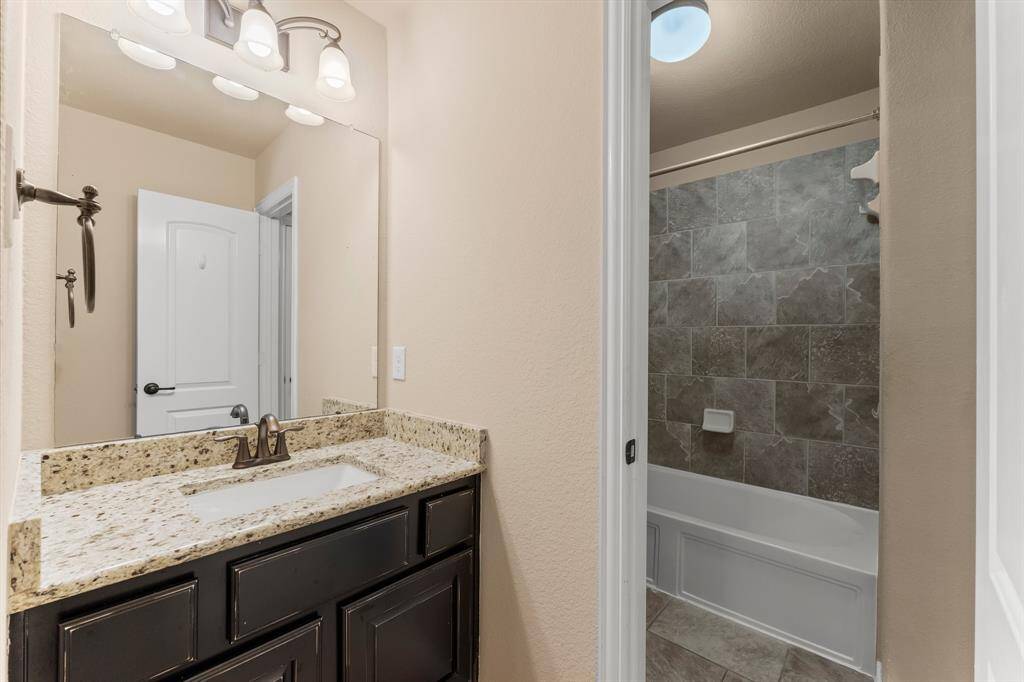 The Jack-and-Jill bathroom for Bedrooms 3 and 4  includes dual rectangular undermount sinks separated for privacy, granite countertops, Versailles tile flooring, hall linen closet, and a private area with toilet and tiled shower/tub combo.