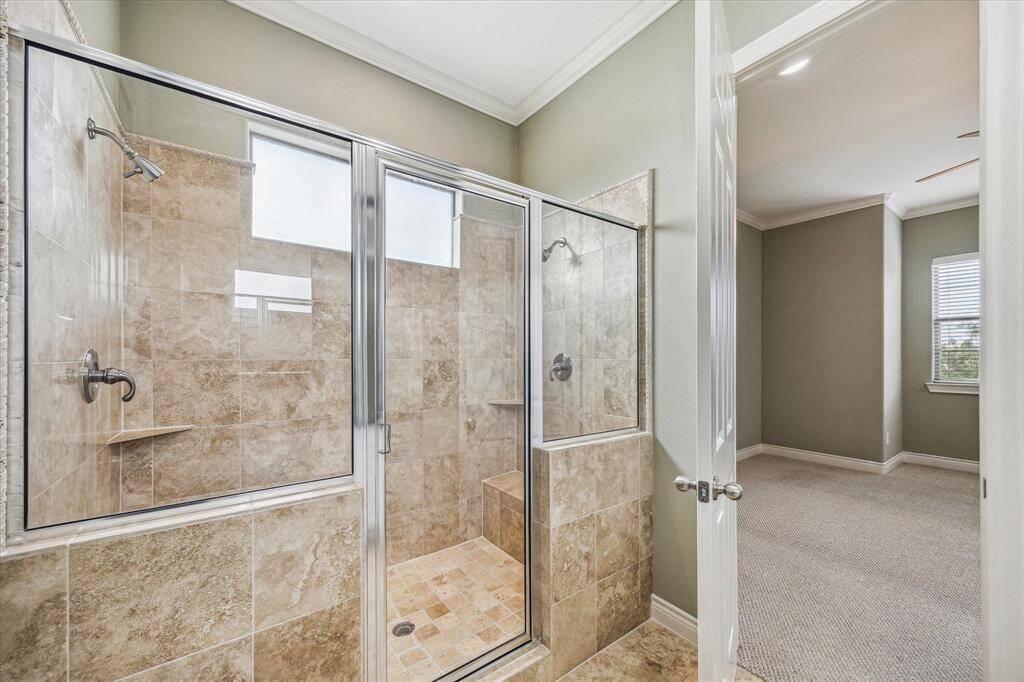 Expansive wall-to-wall primary shower featuring dual shower heads on each end, a framed glass door, and a built-in bench for added comfort. The neutral palette creates a serene, spa-like atmosphere—perfect for unwinding in style.